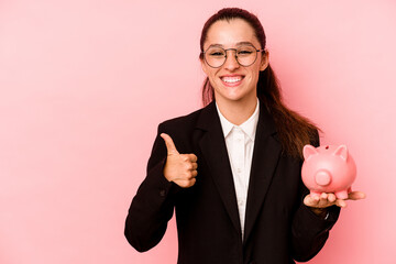 Young business caucasian woman holding piggybank isolated on pink background smiling and raising thumb up