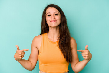 Wall Mural - Young caucasian woman isolated on blue background person pointing by hand to a shirt copy space, proud and confident