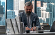 © supamotion - Portrait of 50s adult grey-haired Caucasian businessman signing documents in his office located in a skyscraper, business district buildings in the background