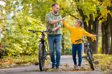 Happy father and daughter walk with bicycles in the autumn park on a sunny day.