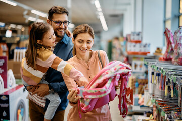 Little girl and her parents choosing backpack for school while shopping in store together.