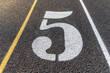 © Thomas - Close up lane number five, 5, on a new black running track with white lane lines and other markings.