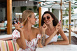 © Анастасия Каргаполов - Two young beautiful smiling hipster female in trendy summer sundress.Smoking vapes electronic devices at outdoor cafe. Positive models having fun