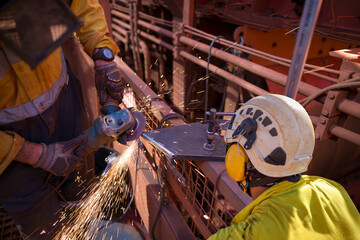 Supervisor construction worker wearing side impact rope access safety white helmet attached with yellow noise disruptive earmuffs protection while worker is performing grinding preparation steel plat 