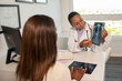 © KAMPUS - Confident doctor showing x-ray picture of lungs and explaining diagnosis to patient. Young African American pulmonologist consulting woman in clinic. Medical consultation, pulmonology concept