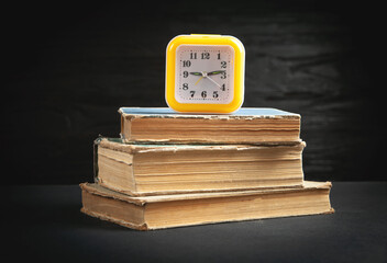 Wall Mural - Yellow clock and books on the black background.