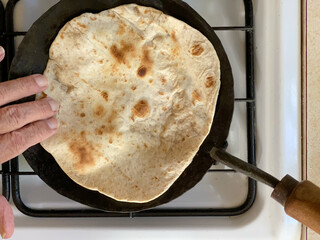 Close-up of a traditional Indian handmade unleavened flat bread, roti or chapati,  made with wheat flour and water is cooking on a black hot disk called tawa. Top view