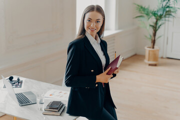 Wall Mural - Professional business woman smiling at camera with notebook in hands