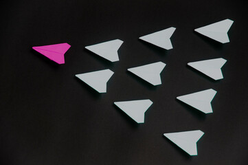 Wall Mural - Purple paper plane origami leading white planes on dark background. Leadership skills concept