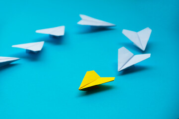 Wall Mural - Yellow paper plane origami leading white planes on blue background. Leadership skills concept
