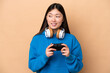 © luismolinero - Young Chinese man playing with a video game controller isolated on beige background looking to the side and smiling