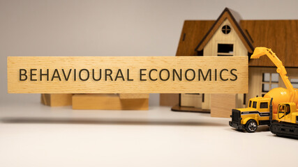 Behavioral economics word written on wooden surface. House and construction concept in background