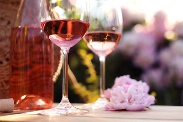 Canvas Print - Bottle and glasses of rose wine near beautiful peony flower on wooden table in garden, closeup