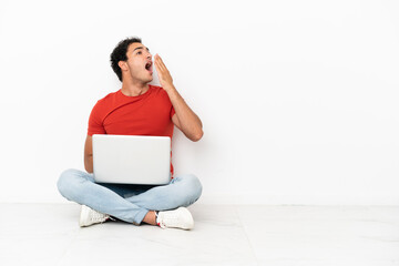 Wall Mural - Caucasian handsome man with a laptop sitting on the floor yawning and covering wide open mouth with hand