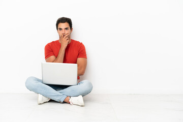 Caucasian handsome man with a laptop sitting on the floor surprised and shocked while looking right