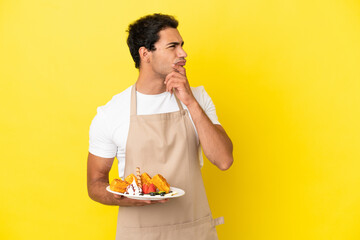 Sticker - Restaurant waiter holding waffles over isolated yellow background and looking up