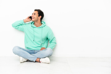 Wall Mural - Caucasian handsome man sitting on the floor keeping a conversation with the mobile phone