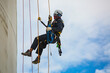 © chitsanupong - Male worker inspection wearing safety first harness rope safety line working at a high place on tank roof spherical gas  blue sky