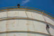 © chitsanupong - Male two worker inspection wearing safety first harness rope safety line working at a high place on tank roof spherical