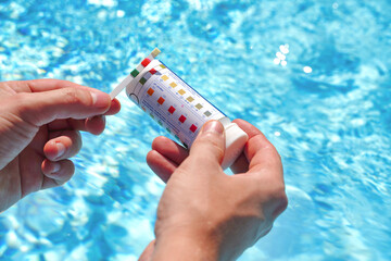 Checking the water quality of a pool with the help of a test strip with PH value, chlorine and algaecide