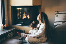Happy Mom And Daughter Resting Near Fireplace At Home.