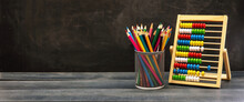 Back To School. Colorful Pencils And Abacus On Blue Wooden Desk, Blackboard Background