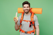 Young Happy Traveler White Man Carry Backpack Stuff Mat Eat Banana Isolated On Plain Green Background. Tourist Leads Active Healthy Lifestyle Walk On Spare Time. Hiking Trek Rest Travel Trip Concept.