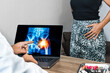 Doctor showing a x-ray of pain in the hips on a laptop. Woman patient in the background