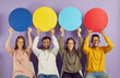 © Studio Romantic - Cheerful young multiracial people sitting in row and holding colored round speech bubbles with copy space. Smiling people holding blank mockup over their heads sitting on chairs on purple background.