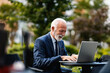 © Dusan Petkovic - A happy senior businessman sits at the cafe terrace and finishes his report on the laptop. Hands are on the keyboard.