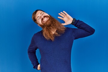 Canvas Print - Redhead man with long beard wearing casual blue sweater over blue background stretching back, tired and relaxed, sleepy and yawning for early morning