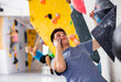 © JackF - European young man having telephone conversation while grabbing ledges of artificial climbing wall in bouldering centre.