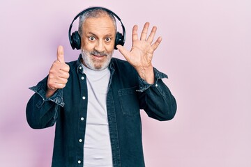 Poster - Handsome senior man with beard listening to music using headphones showing and pointing up with fingers number six while smiling confident and happy.