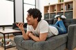 © Krakenimages.com - Young hispanic man talking on the smartphone lying on the sofa at home.