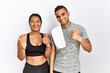 Young latin couple wearing sportswear standing over isolated background success sign doing positive gesture with hand, thumbs up smiling and happy. cheerful expression and winner gesture.