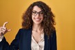© Krakenimages.com - Hispanic woman with curly hair standing over yellow background smiling and confident gesturing with hand doing small size sign with fingers looking and the camera. measure concept.