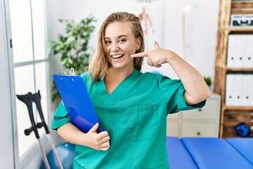 Canvas Print - Young caucasian woman working at pain recovery clinic smiling cheerful showing and pointing with fingers teeth and mouth. dental health concept.