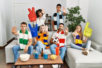 Sticker - Group of friends supporting football team watching tv al home sitting on the sofa with open hand doing stop sign with serious and confident expression, defense gesture