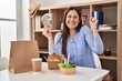 © Krakenimages.com - Young brunette woman eating take away food at home holding money screaming proud, celebrating victory and success very excited with raised arm