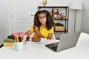 Poster - Young african american girl doing homework at home pointing with hand finger to the side showing advertisement, serious and calm face