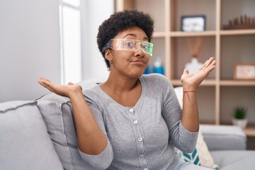 Sticker - Young african american woman wearing virtual reality glasses sitting on the sofa shouting and screaming loud to side with hand on mouth. communication concept.