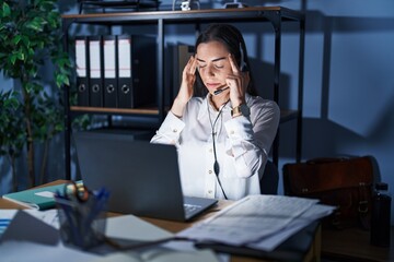 Canvas Print - Young brunette woman wearing call center agent headset working late at night with hand on head for pain in head because stress. suffering migraine.