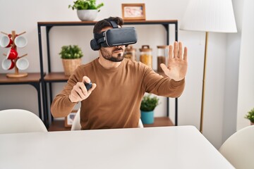 Young hispanic man playing video game using virtual reality glasses at home