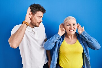 Sticker - Young brazilian mother and son standing over blue background trying to hear both hands on ear gesture, curious for gossip. hearing problem, deaf