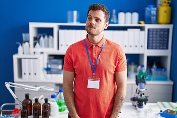 Poster - Young hispanic man working at scientist laboratory smiling looking to the side and staring away thinking.