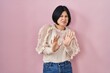 Young asian woman standing over pink background disgusted expression, displeased and fearful doing disgust face because aversion reaction. with hands raised