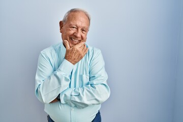 Poster - Senior man with grey hair standing over blue background looking confident at the camera smiling with crossed arms and hand raised on chin. thinking positive.