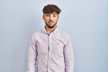 Sticker - Arab man with beard standing over blue background relaxed with serious expression on face. simple and natural looking at the camera.