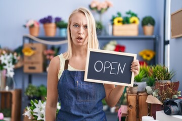 Poster - Young caucasian woman working at florist with open sign scared and amazed with open mouth for surprise, disbelief face