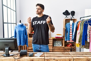 Wall Mural - Young hispanic man working at retail boutique doing money gesture with hands, asking for salary payment, millionaire business